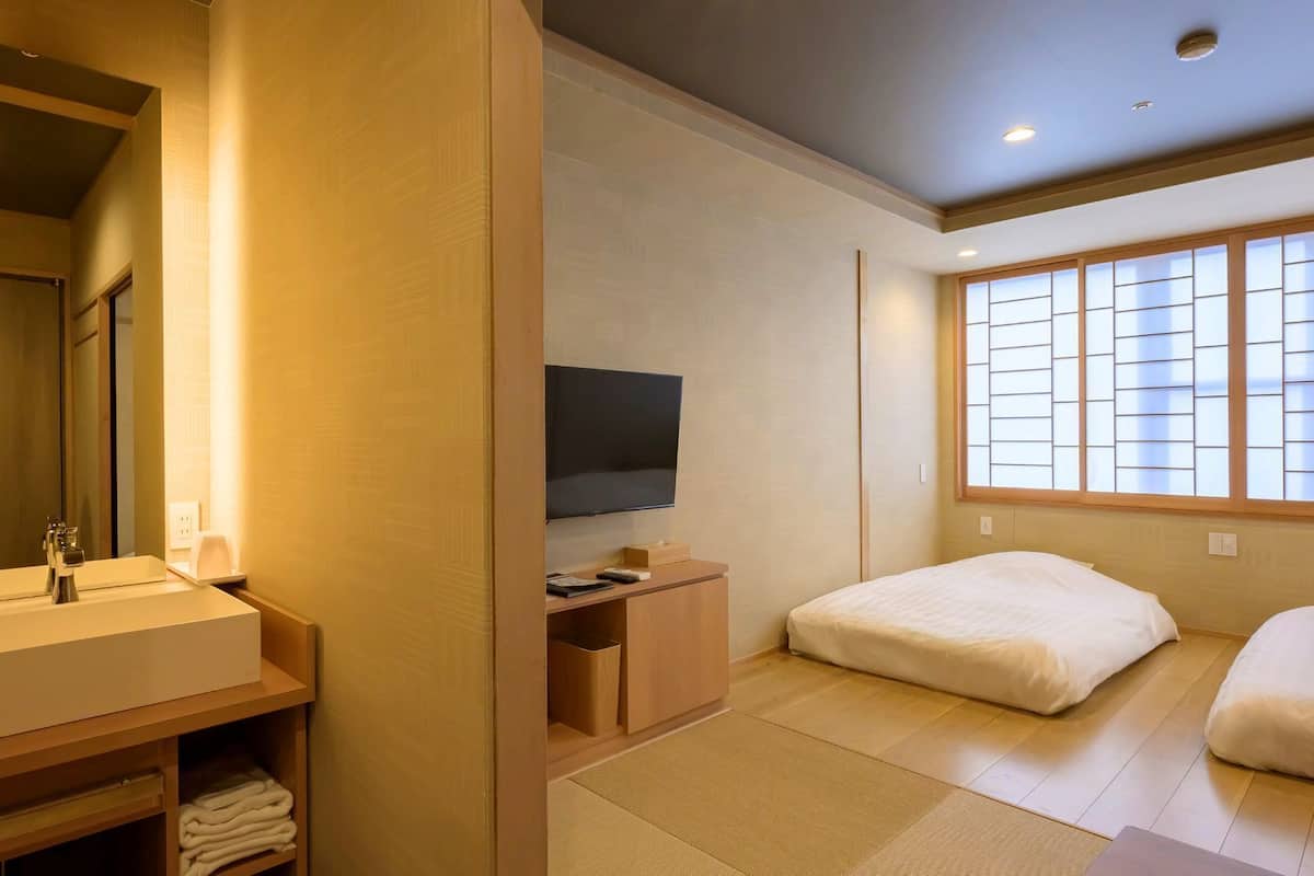 Habitación de hotel con tocador de madera, televisión de pantalla plana, cama y ventana con paneles shoji.