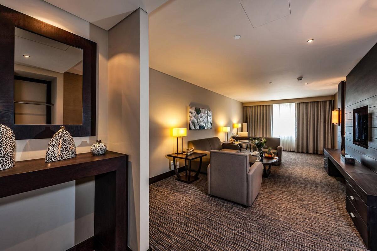 A hotel room with a large bed, a seating area with a sofa and armchairs, a TV, and a desk with a lamp.