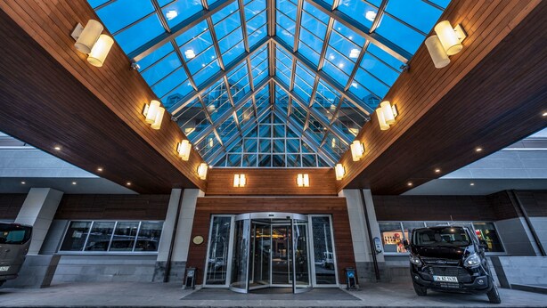 A hotel entrance with a glass ceiling, a revolving door, and a parked car.