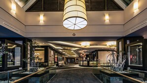 A modern hotel lobby with a central chandelier, glass railings, and a reception desk.