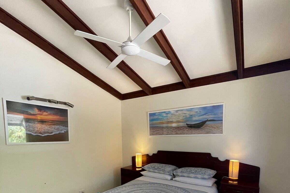 A bedroom with a bed, two bedside tables, a ceiling fan, and two wall-mounted lamps.