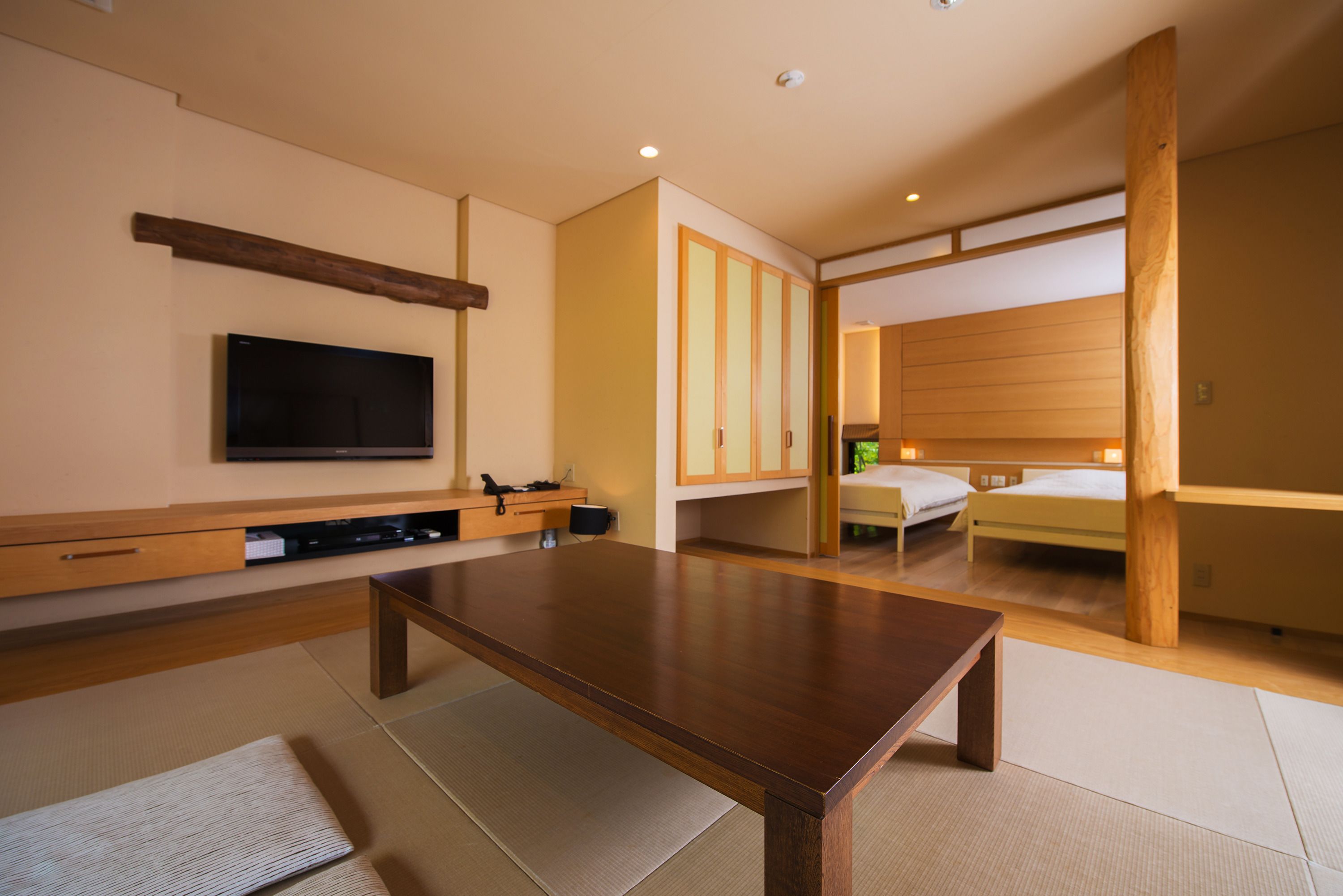 Une chambre d’hôtel moderne avec un plancher en bois, des tatamis, un téléviseur à écran plat, un lit et une armoire en bois.