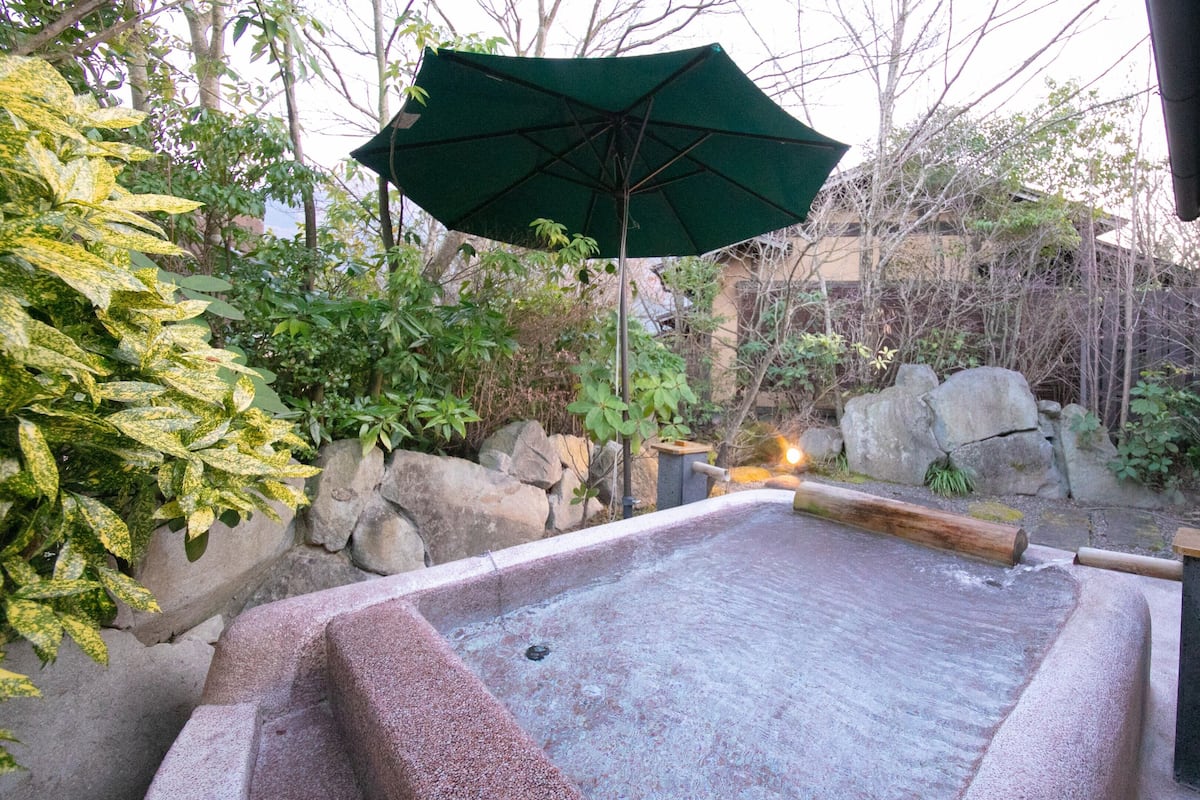 Un jacuzzi con borde de piedra, rodeado de rocas y plantas.