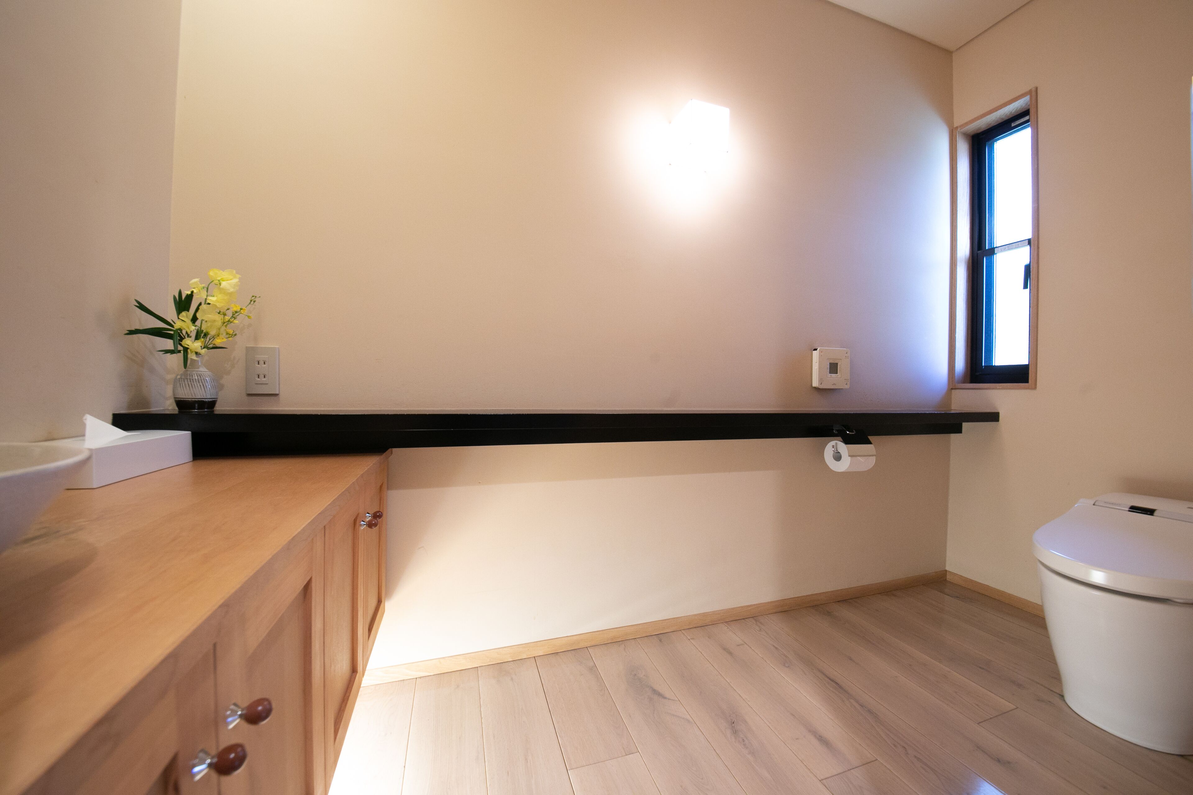 A bathroom with a wooden vanity, a toilet, a window, and a wall-mounted light fixture.