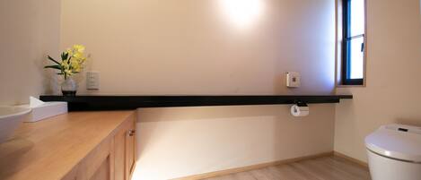 A bathroom with a wooden vanity, a toilet, a window, and a wall-mounted light fixture.