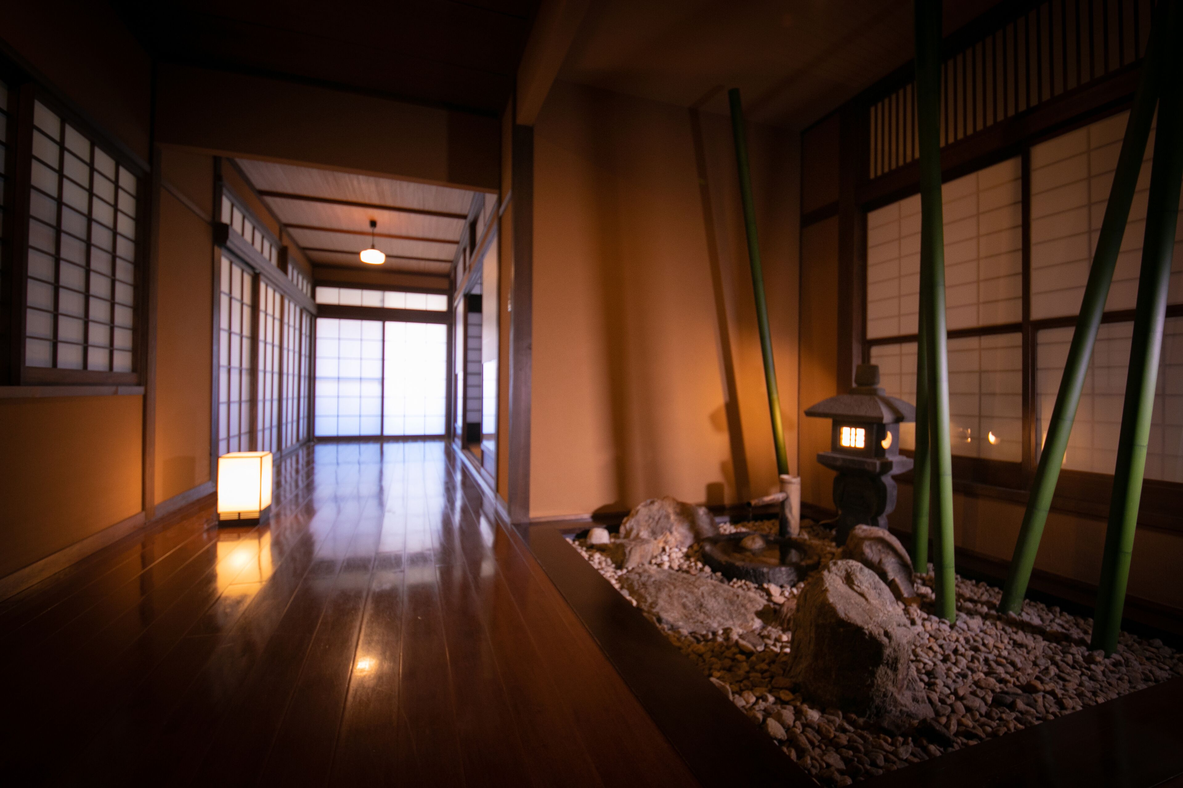 A corridor with wooden flooring, traditional Japanese sliding doors, and a stone lantern.
