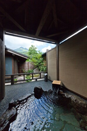 A traditional Japanese onsen with a wooden cabin, a stone bath, and a view of mountains. - Yufuin Bettei Itsuki (Yufu)