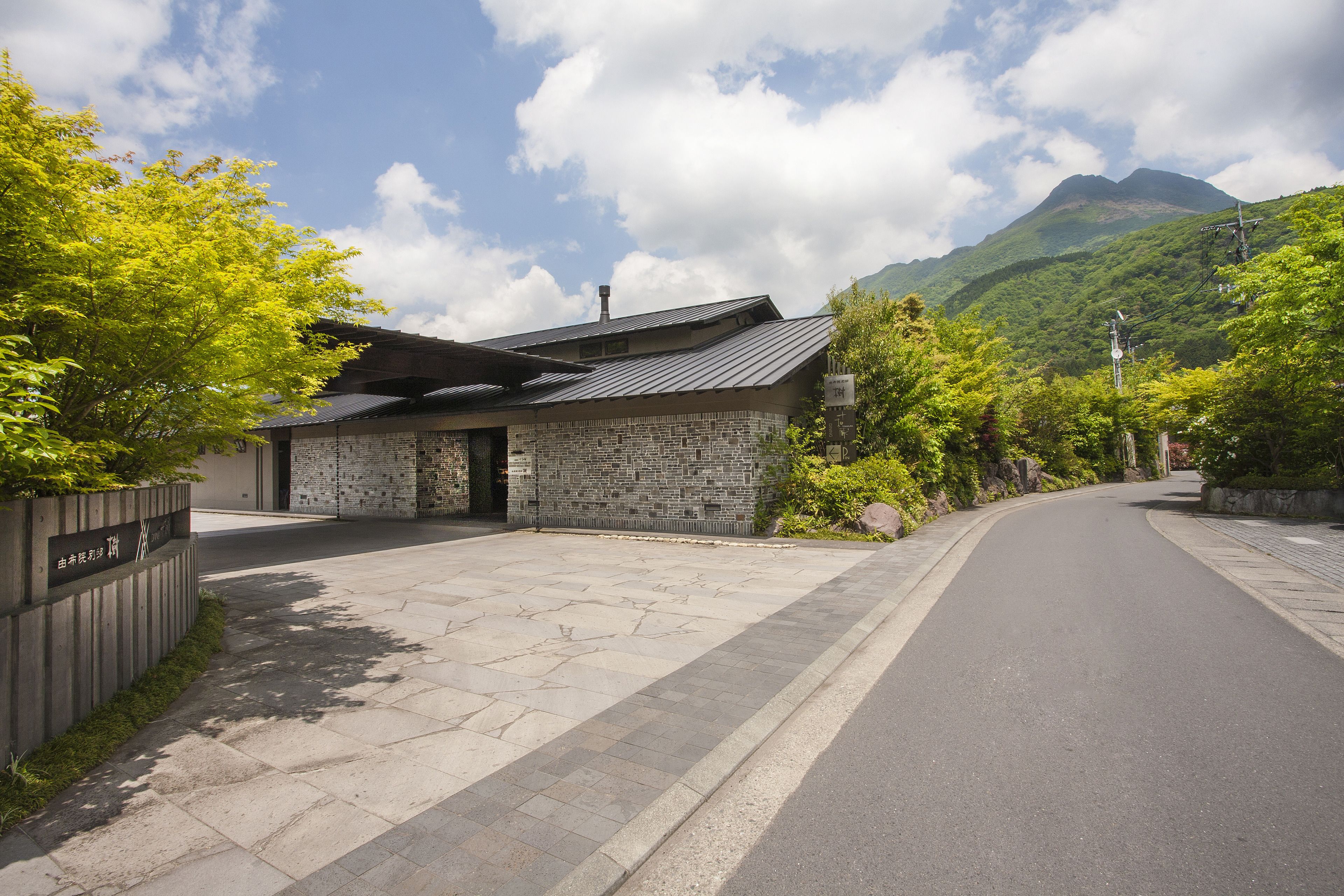 A stone building with a sloped roof, a paved driveway, and a mountain in the background.