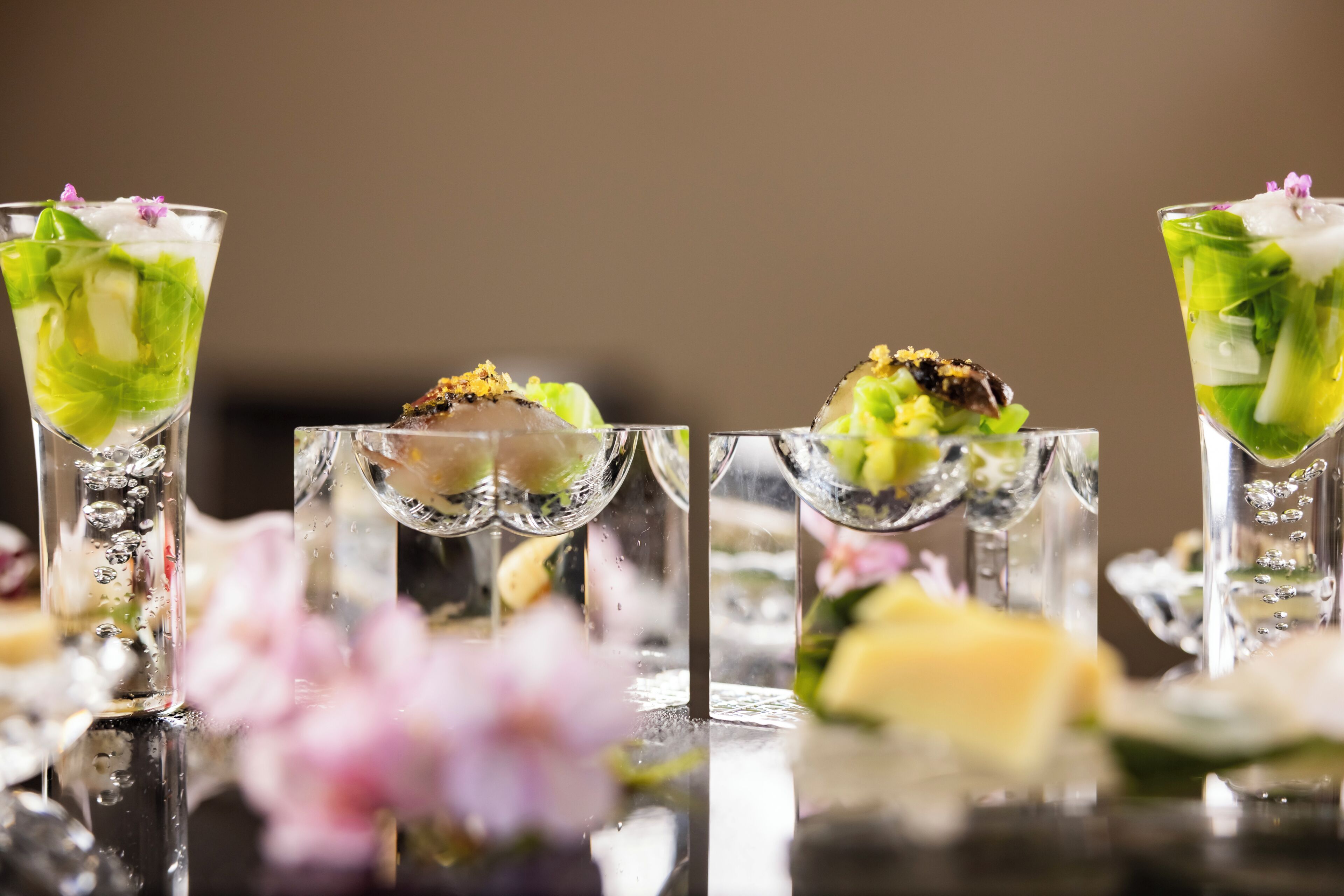 A series of elegantly presented drinks with garnishes, set on a reflective surface with a blurred background.