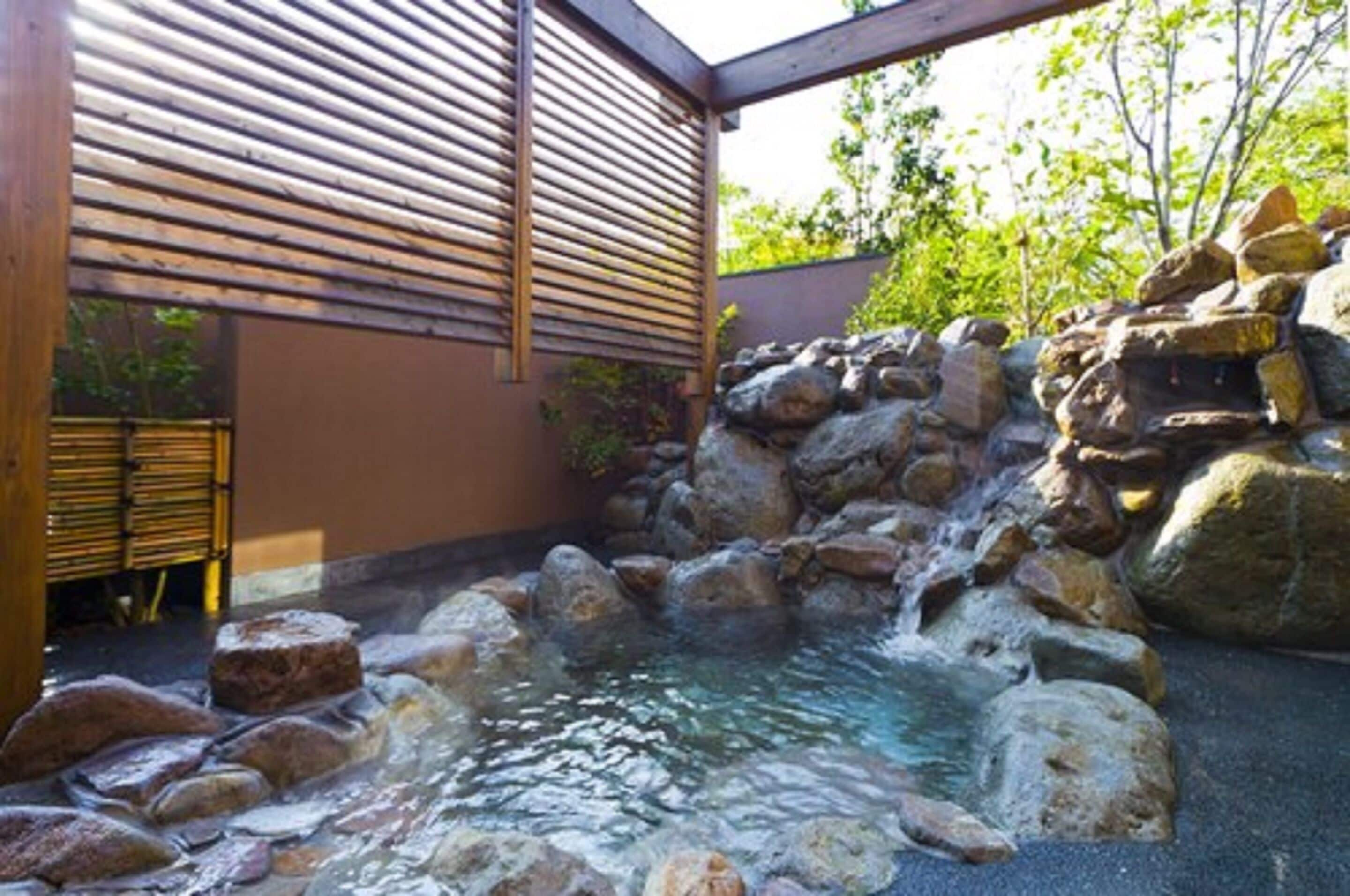 A hot spring area with a wooden pergola, stone rocks, and a small waterfall.