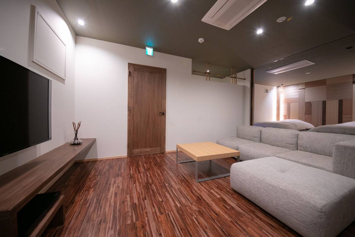 A modern living room with a wooden floor, a sofa, a TV on a wooden stand, and a small table.
