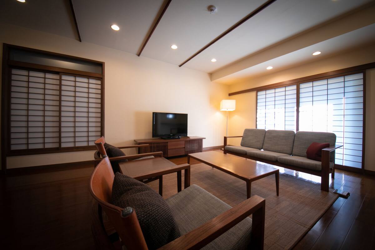 A traditional Japanese-style living room with tatami flooring, a low wooden table, a sofa, and a television.