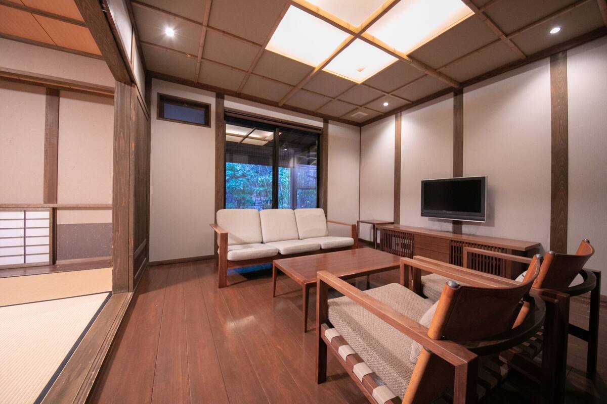 A traditional Japanese-style room with tatami flooring, a low wooden table, a sofa, and a television.