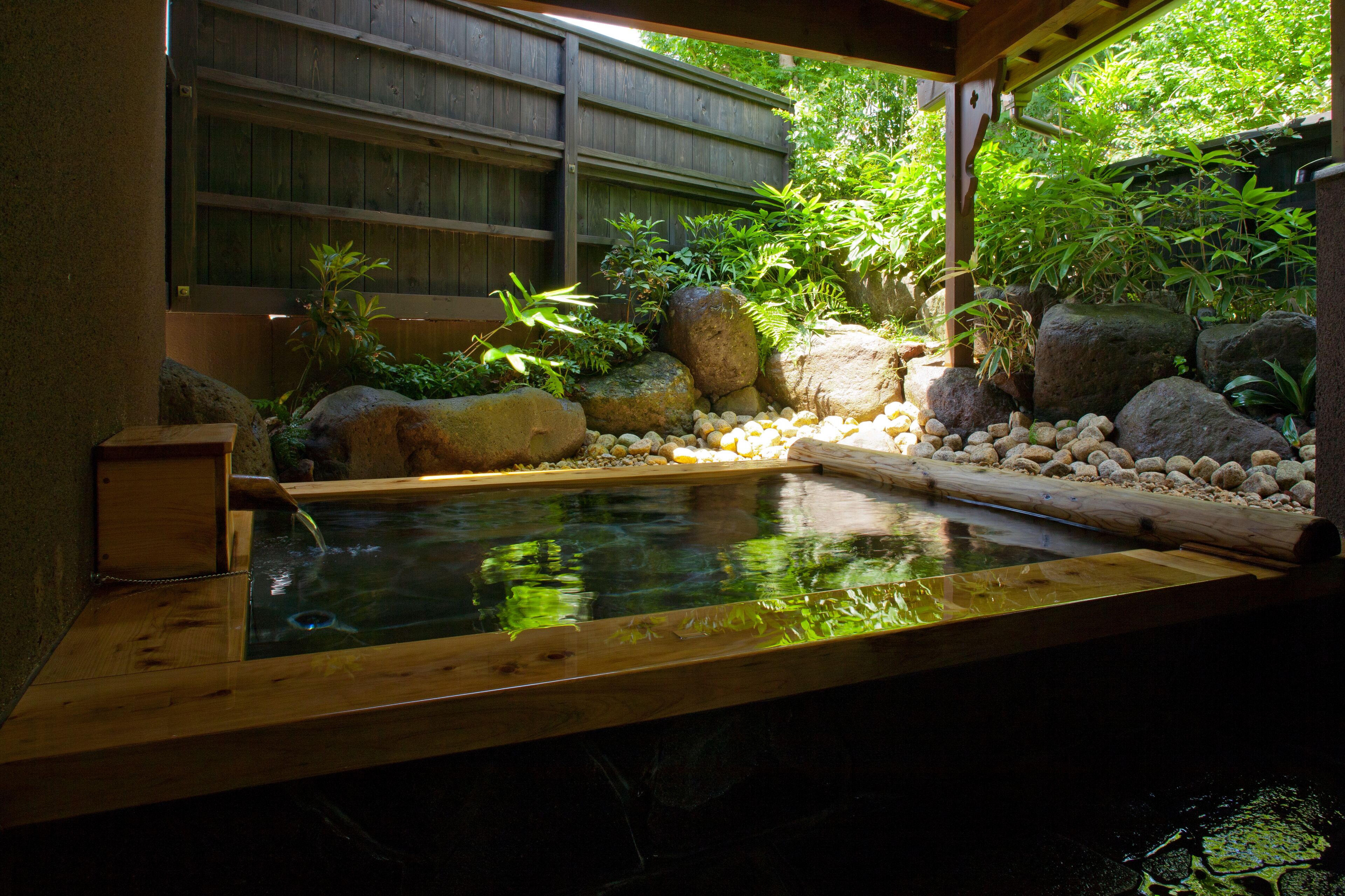 A traditional Japanese onsen with a wooden bath, surrounded by rocks and greenery.
