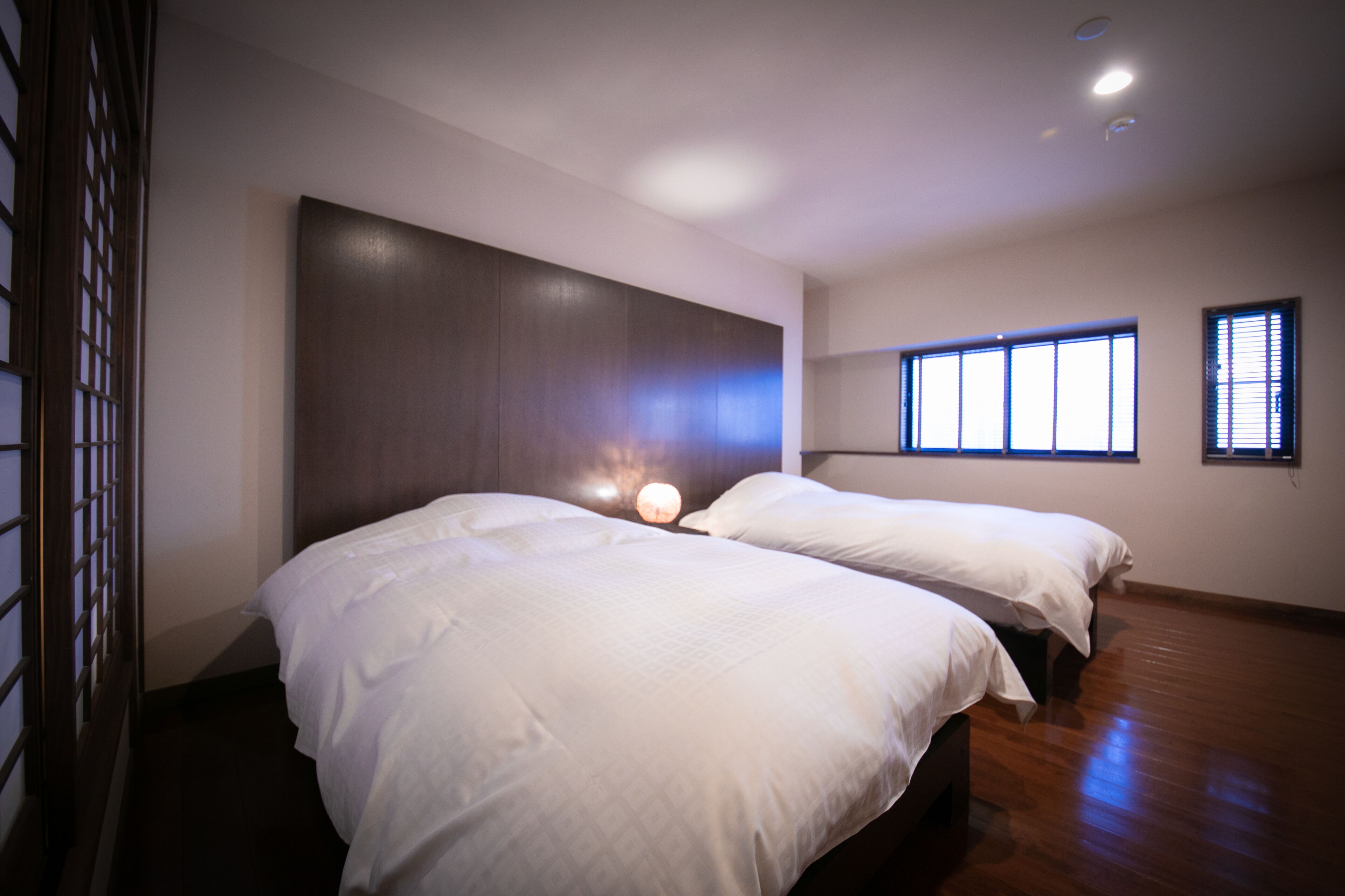 A hotel room with two beds, a large window, and a wooden floor.