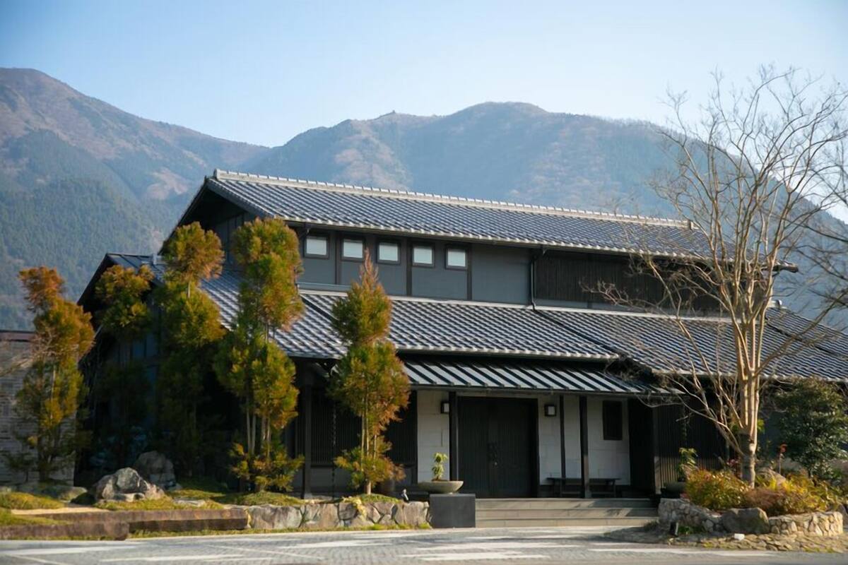 A traditional Japanese building with a tiled roof, surrounded by trees and mountains.