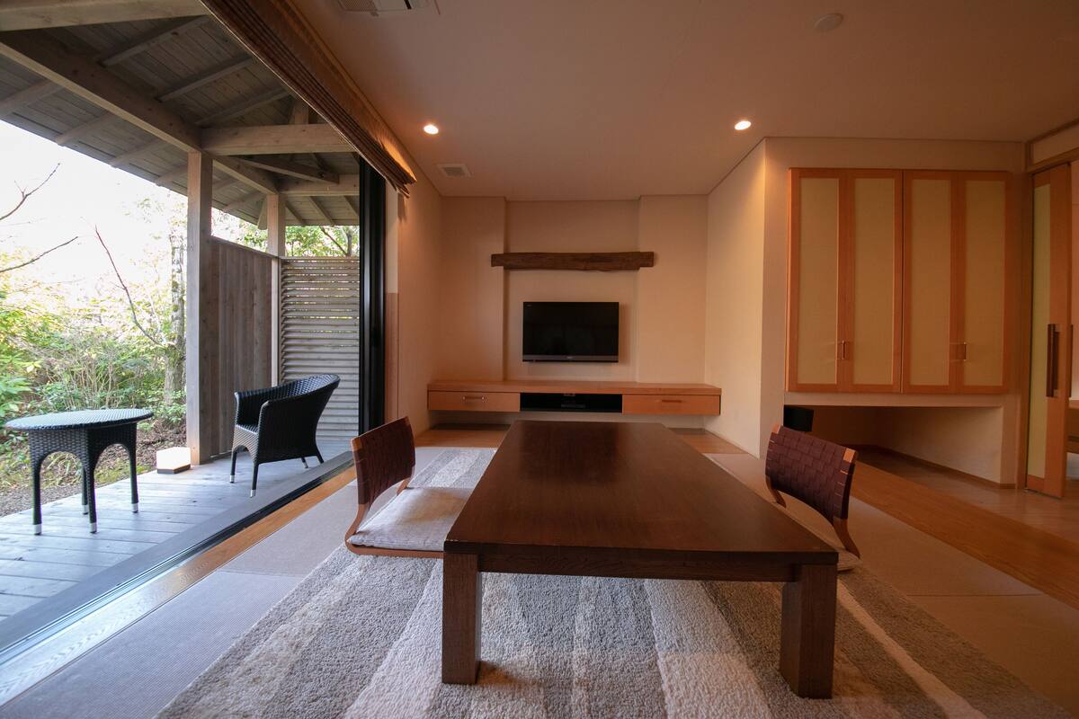 A spacious dining area with a large wooden table, comfortable chairs, a flat-screen TV mounted on the wall, and a sliding glass door leading to an outdoor patio.