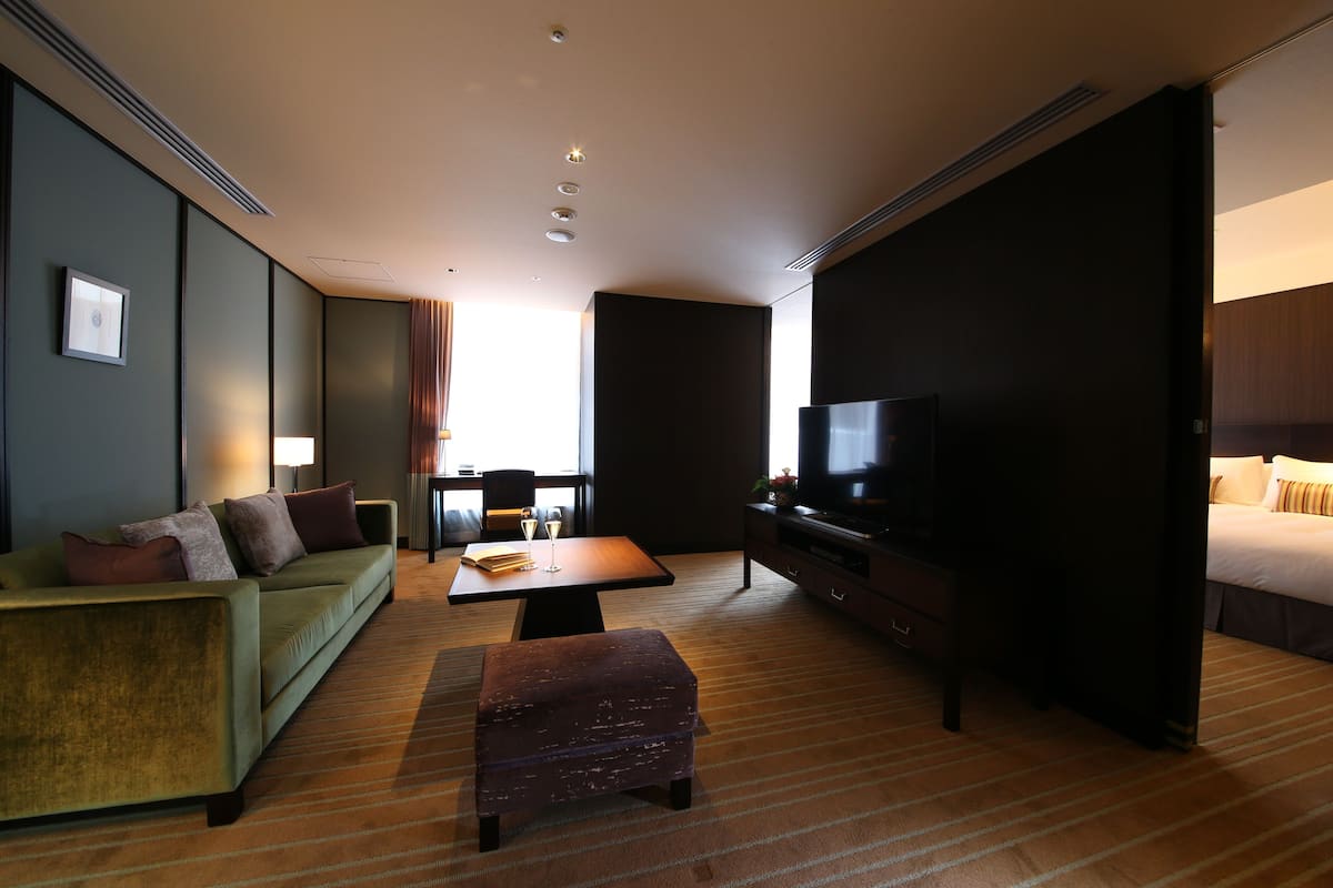 Una camera d'hotel con un divano verde, un tavolino in legno, una televisione e un letto.