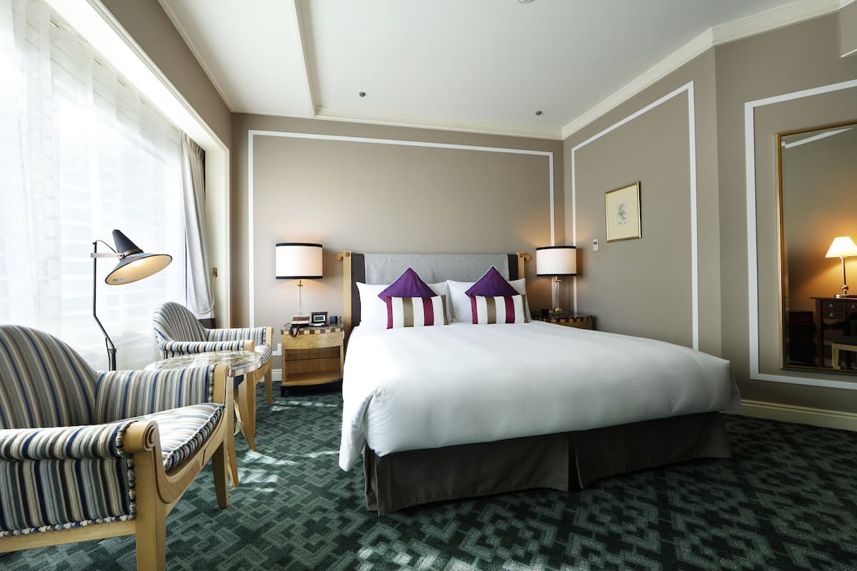 Una camera d'albergo con un letto grande, due comodini, una poltrona, una scrivania e uno specchio ampio.