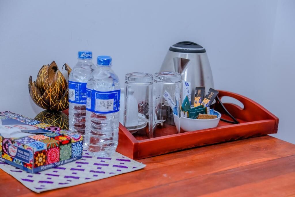 A tray with a kettle, two bottles of water, salt and pepper shakers, a bowl of snacks, and a decorative item on a wooden table.