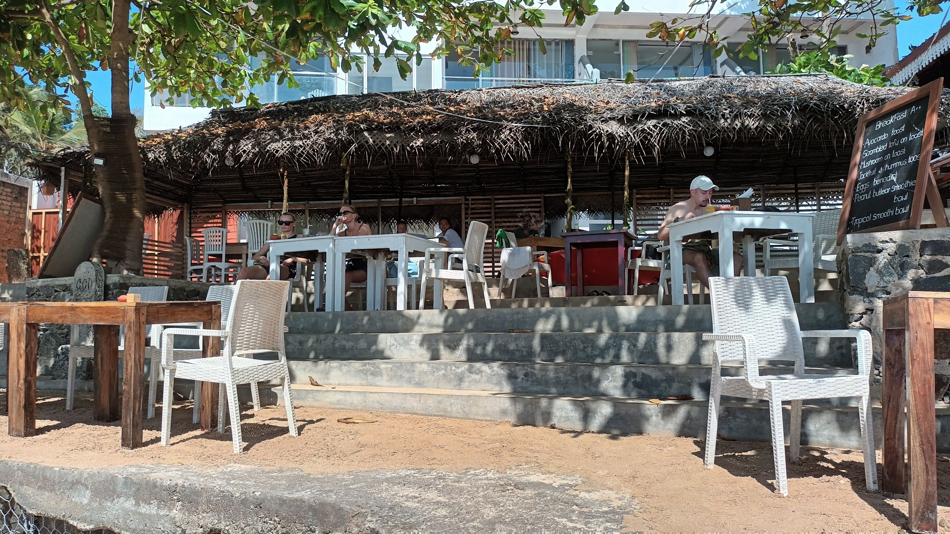 An outdoor café with thatched roofing, white plastic chairs, and a stone wall.