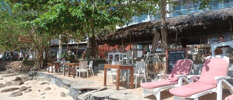 A beachside seating area with lounge chairs and tables, a thatched-roof structure, and a sign indicating a coral beach.