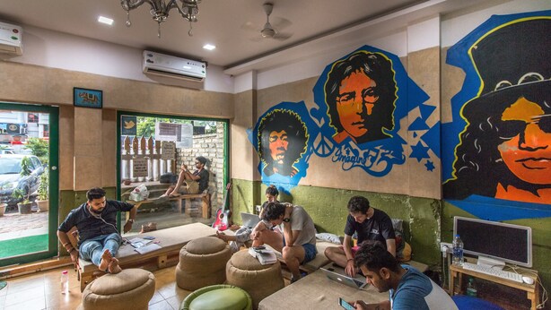 A room with four people sitting on ottomans, a laptop on a table, and a mural on the wall. - Backpacker Panda Appetite Mumbai (Mumbai)