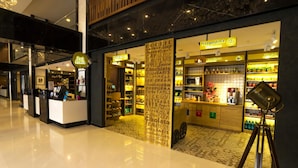 Uma área comercial moderna em ambiente interno, com diversas opções de alimentação e bebidas, incluindo uma loja de noodles e uma cafeteria.