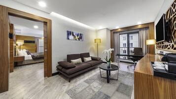 A modern hotel room with a sofa, a coffee table, a TV, and a balcony with curtains.