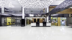 Um hall amplo com uma recepção moderna, teto alto com luminárias pendentes e piso limpo e bem cuidado.