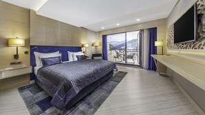 Quarto de hotel moderno com uma cama grande, varanda com vista para a cidade e televisão de tela plana na parede.
