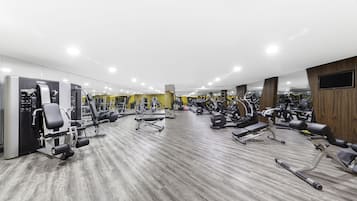 Une salle de sport moderne équipée de divers appareils d’exercice, dotée de murs recouverts de miroirs et d’un plancher en bois.