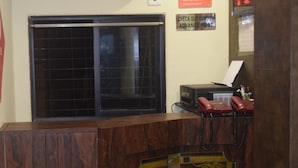 Un comptoir d’accueil d’hôtel avec un plan de travail en bois, un téléphone rouge et une horloge numérique affichant l’heure.
