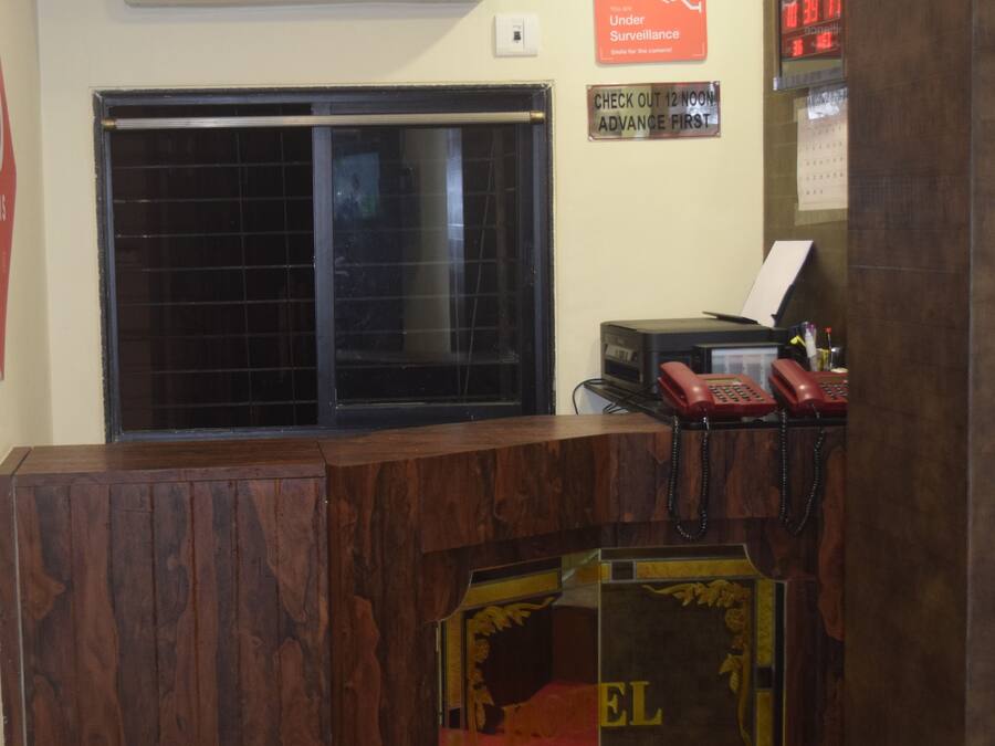 A hotel reception desk with a wooden counter, a red telephone, and a digital clock displaying the time.