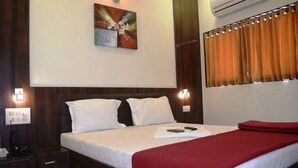 Une chambre d’hôtel avec un grand lit, une table de chevet, une lampe fixée au mur et un tableau au-dessus du lit.