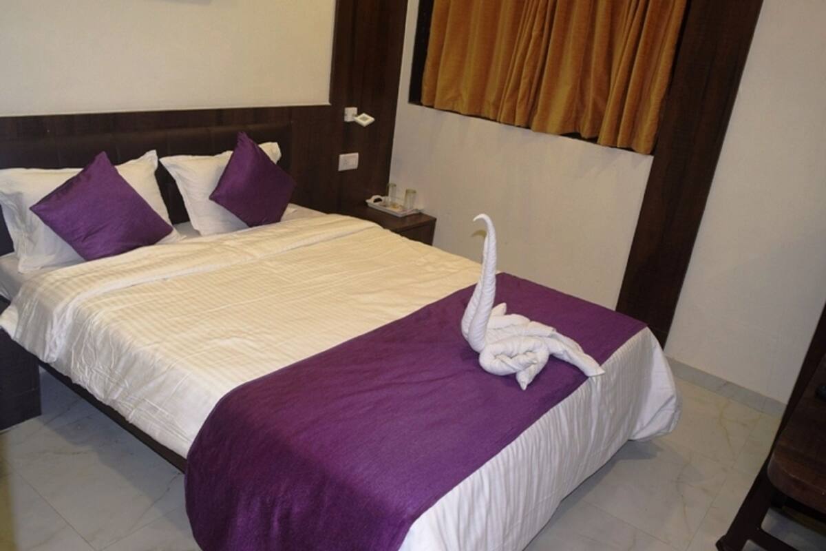 A neatly made bed with a purple blanket and a white swan-shaped towel.