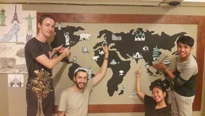 Eine Gruppe von Personen steht vor einer Weltkarte mit verschiedenen Symbolen.