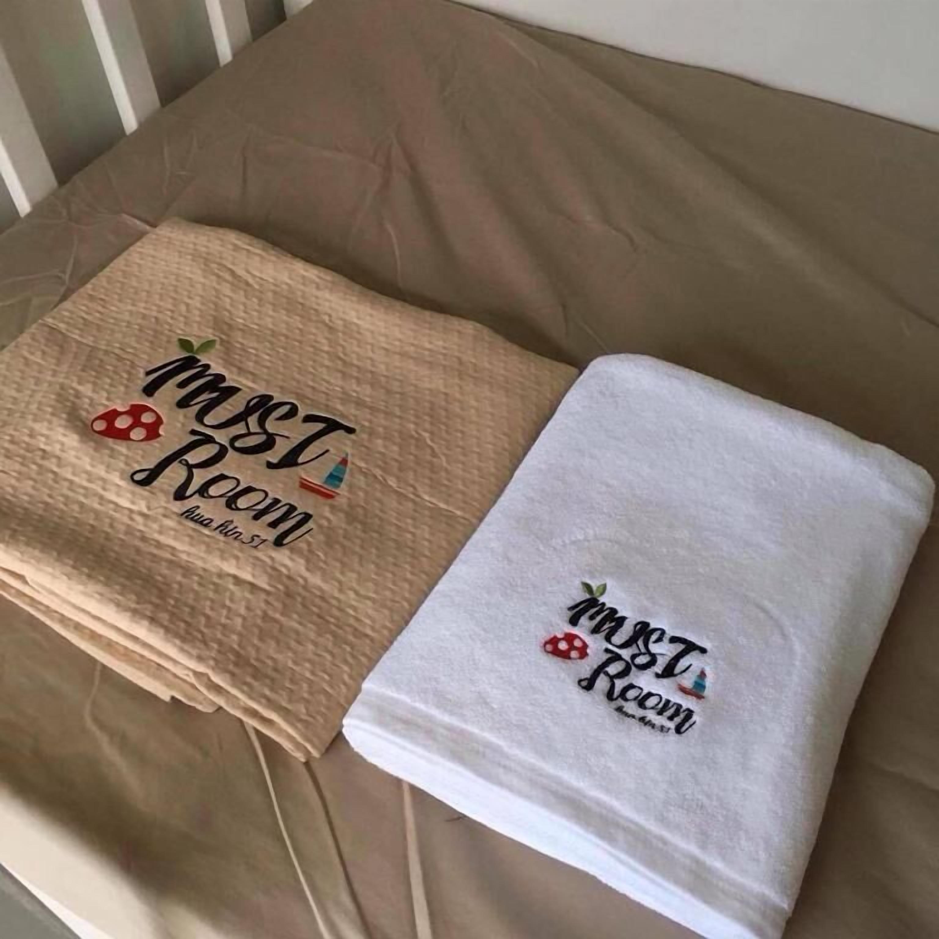 Dos toallas con bordados y motivos de fresas sobre una cama color beige.