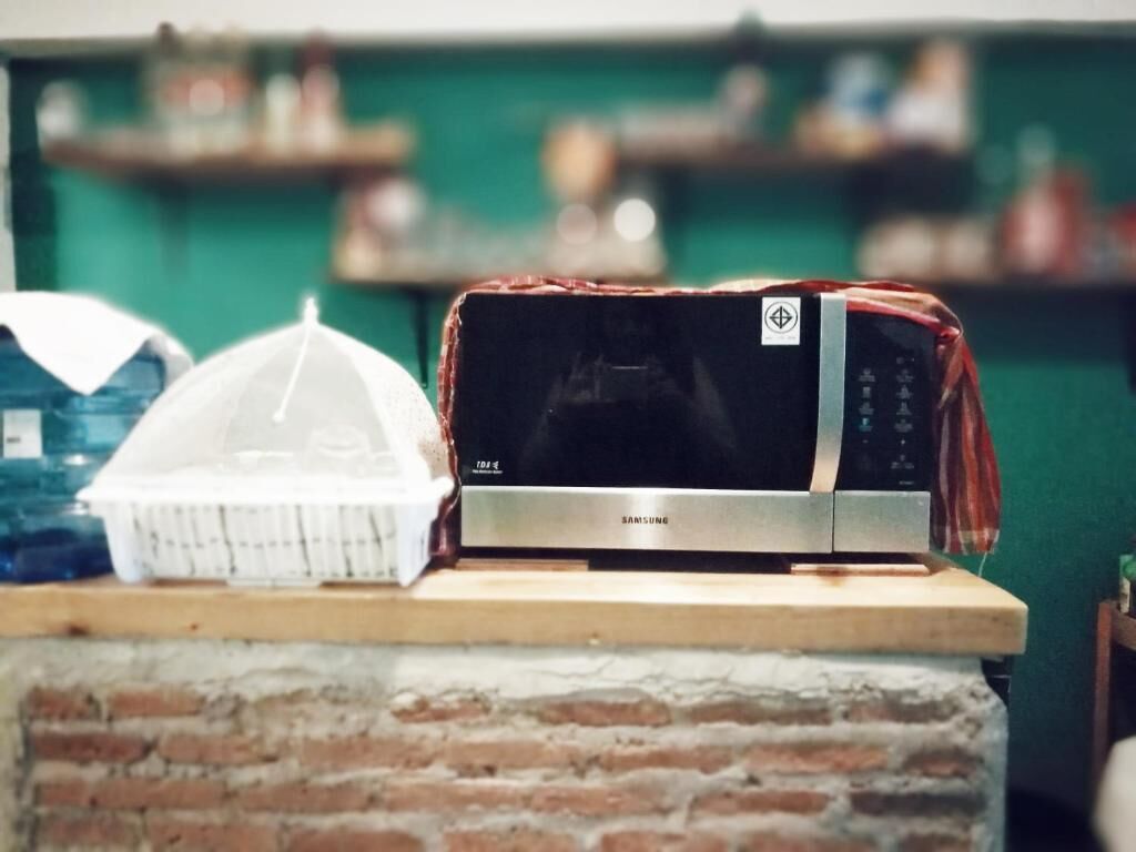 A microwave on a brick counter with a white container and a white umbrella in the background.