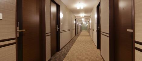 Un couloir d’hôtel avec des revêtements de sol en moquette et des portes en bois.