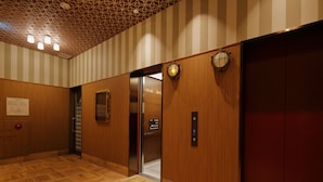 Interior de un ascensor con paredes de madera, techo estampado y suelo de baldosas.
