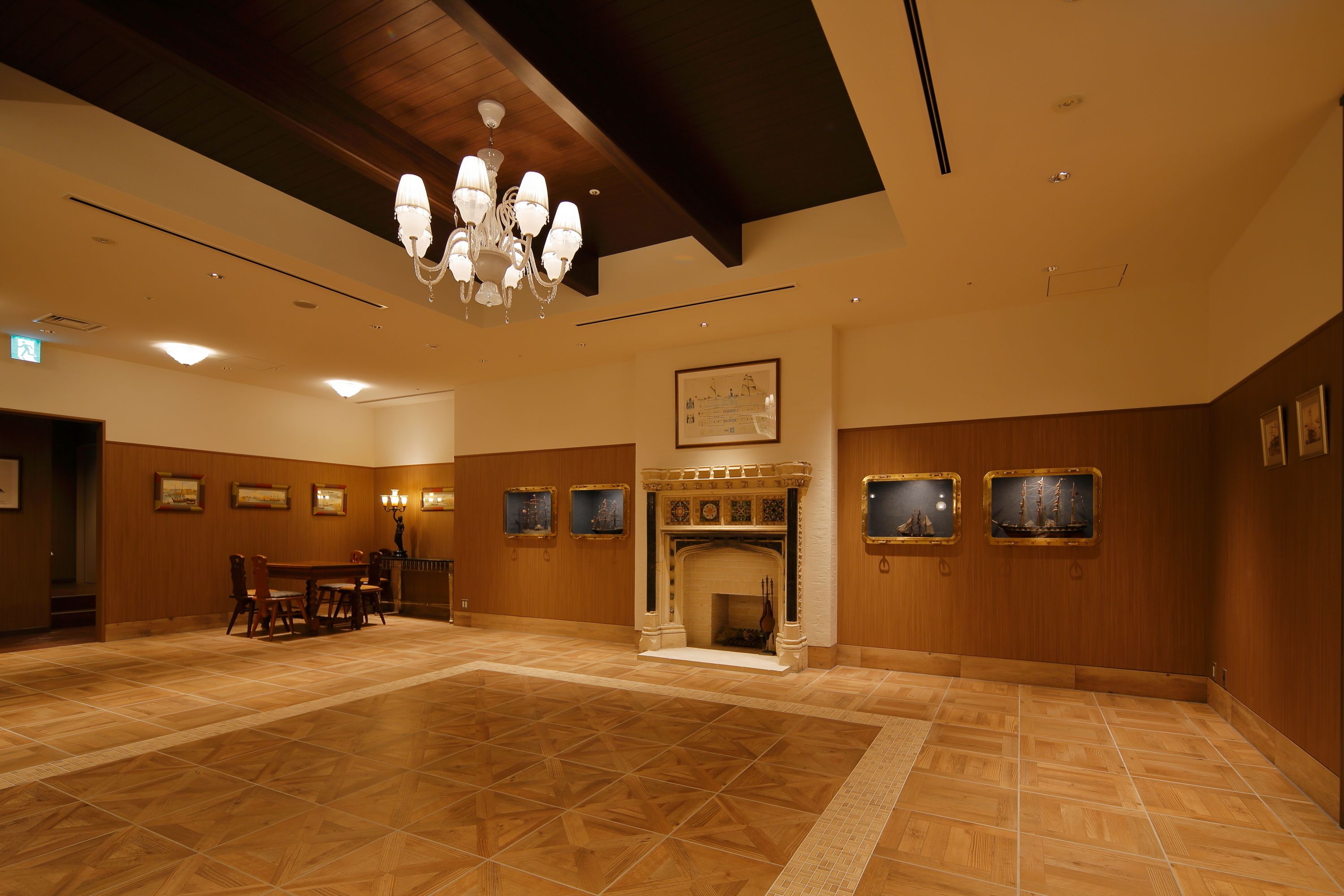 A spacious lobby with a wooden floor, a chandelier, a fireplace, and framed pictures on the walls.