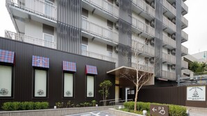 Un edificio moderno con varios balcones, un letrero que indica una zona de estacionamiento y un pequeño árbol al frente.