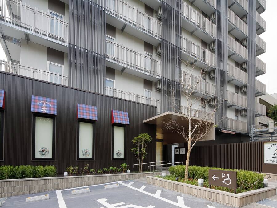 A modern building with multiple balconies, a sign indicating a parking area, and a small tree in the foreground.