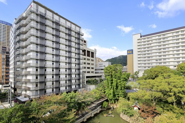 A multi-story hotel with balconies, a river, and a small shrine.