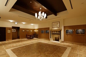 A spacious room with a wooden floor, a chandelier, a fireplace, and framed pictures on the walls.
