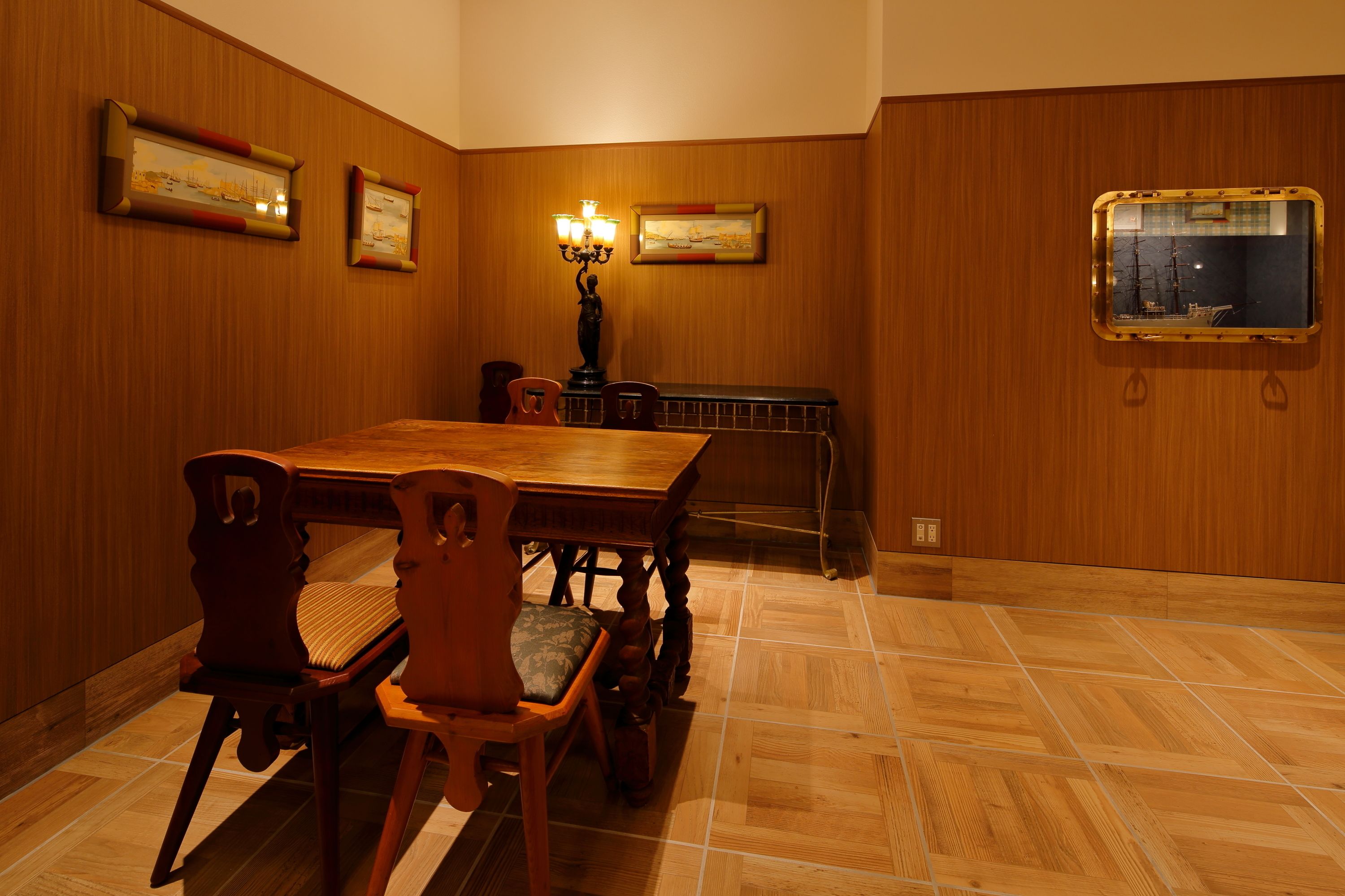 Un comedor con una mesa y sillas de madera, obras de arte enmarcadas en las paredes y un barco en la ventana.