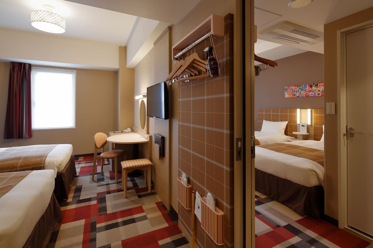Une chambre d’hôtel avec deux lits, un bureau, une chaise, une télévision et une salle de bain avec douche et toilettes.