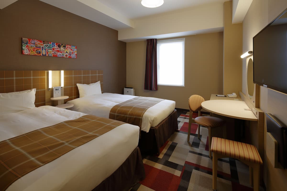 Une chambre d’hôtel avec deux lits, un bureau, une chaise, une télévision et une fenêtre avec des rideaux.