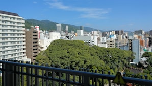 Un paisaje urbano con una mezcla de edificios modernos y tradicionales, un árbol destacado en primer plano y un cielo azul despejado.